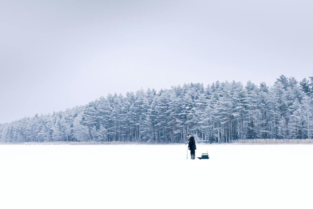 A serene winter landscape with a person ice fishing on a frozen lake in Saint Petersburg.