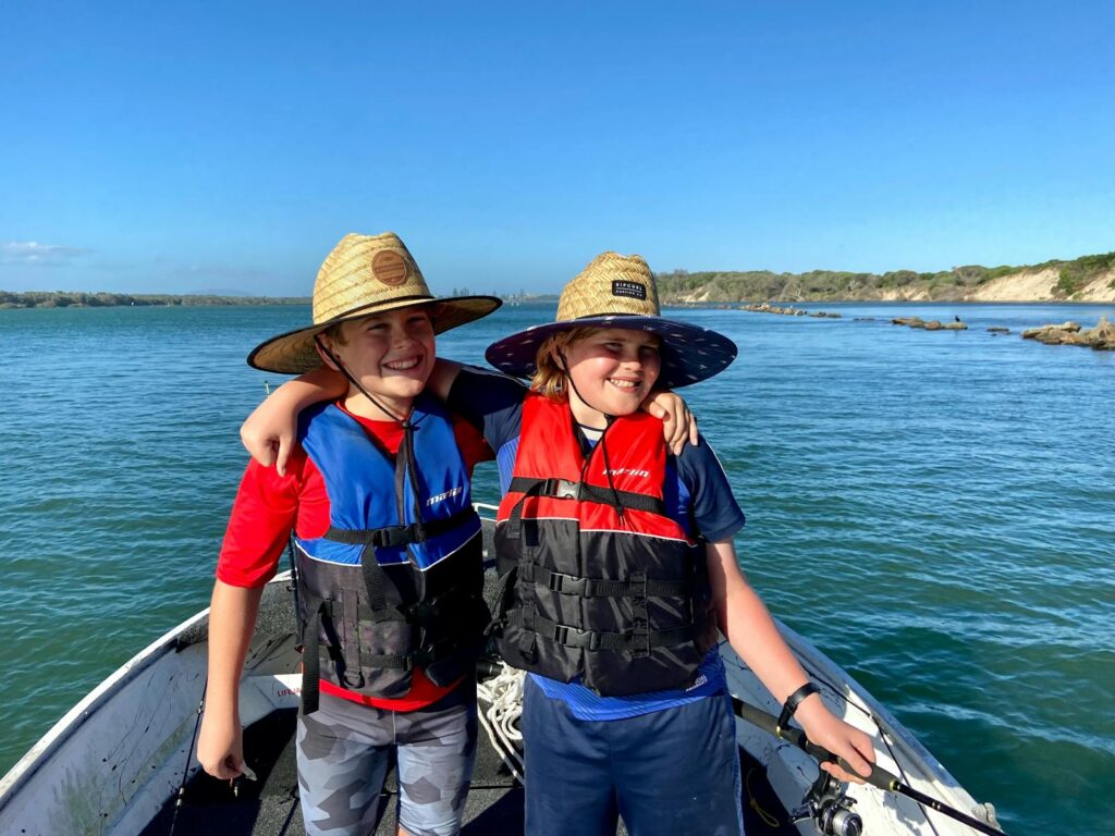 Two children smiling and enjoying a sunny day boating on the water.