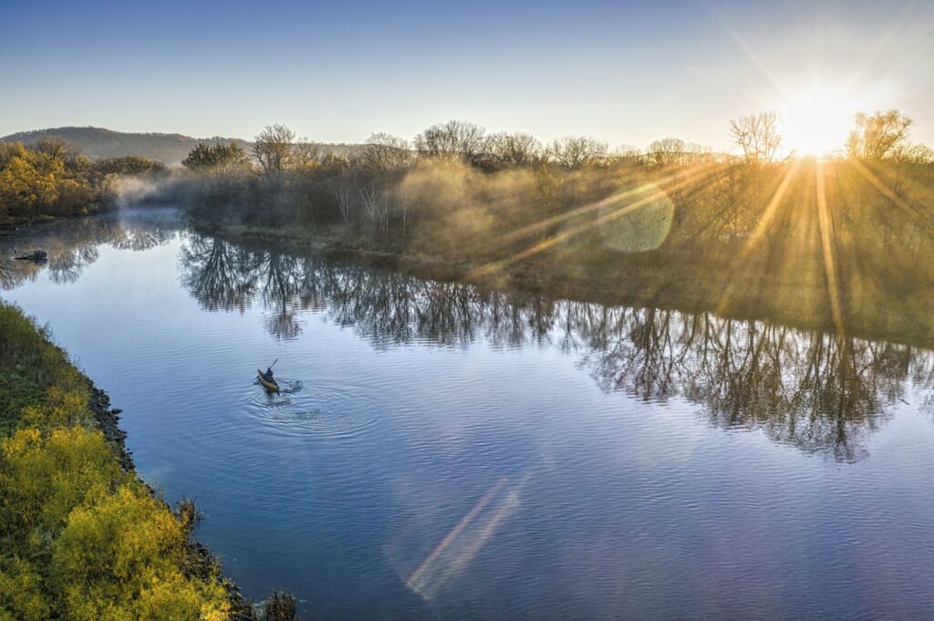 Peaceful aerial view of a river at sunrise with fog and reflections, capturing nature's beauty.