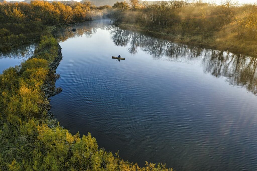 A peaceful autumn scene of a lone kayaker on a calm lake surrounded by colorful fall foliage.