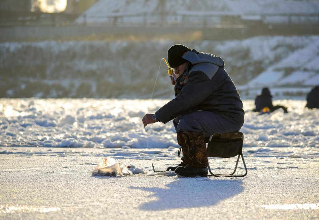 A man enjoys ice fishing on a frozen lake in snowy Kemerovo, Russia, during winter.