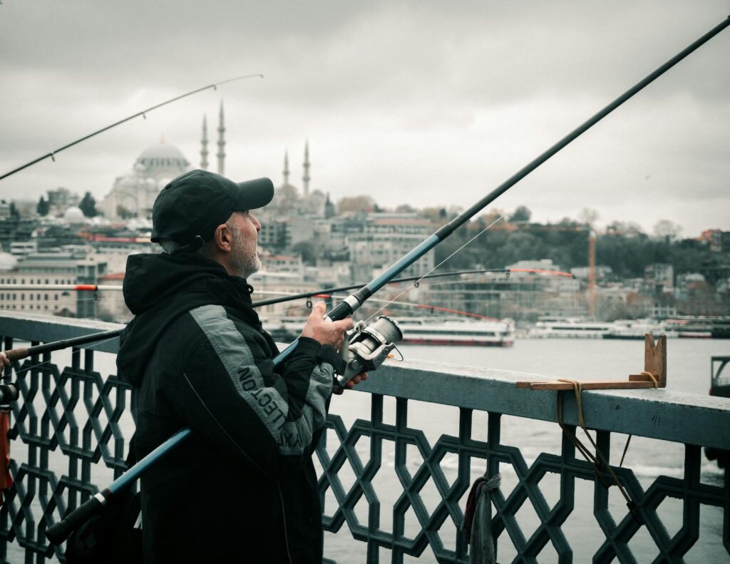 Man fishing on Galata Bridge, İstanbul with city skyline backdrop.