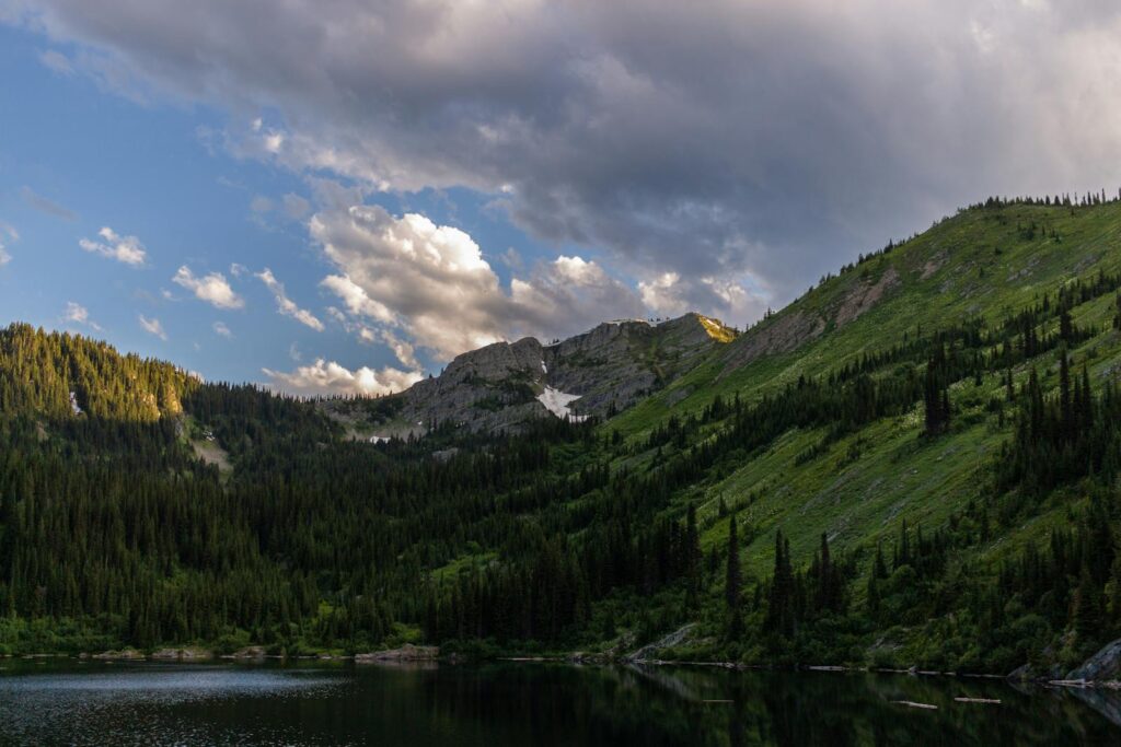 Sunset view of serene alpine mountains with lush forests and reflecting lake, perfect for travel and nature backgrounds.