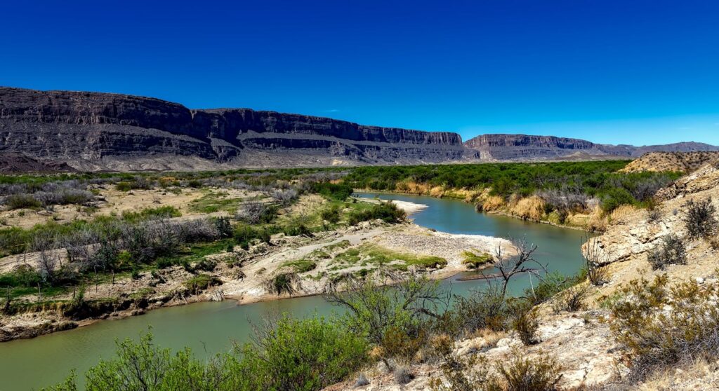 Majestic river winding through desert landscape with mountains under clear blue sky.