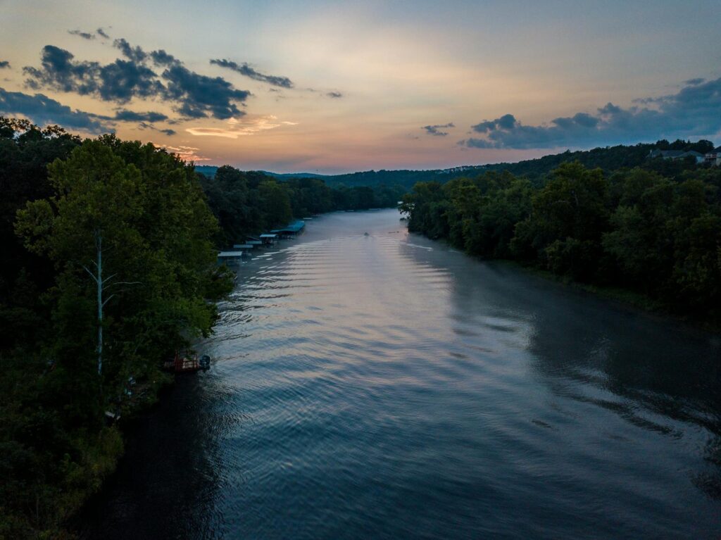 Aerial view of a serene river with lush trees at sunrise, capturing nature's tranquility in Hollister, Missouri.