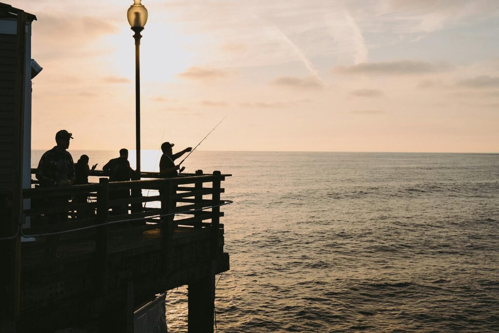 Silhouetted figures fishing on a pier during a breathtaking ocean sunset.