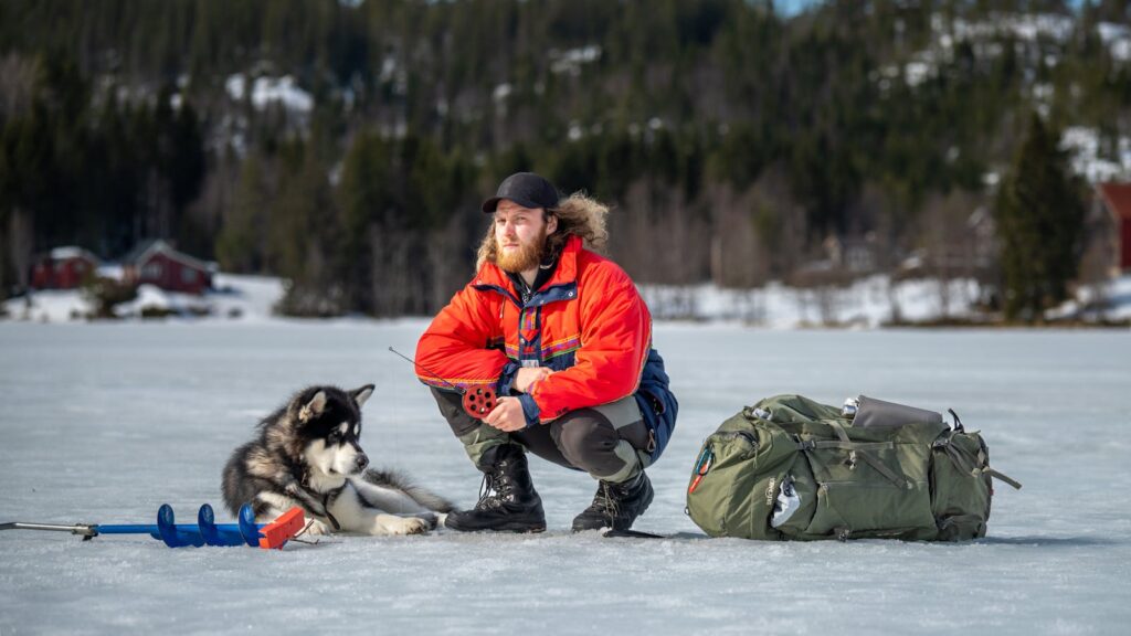 A man and his husky enjoy a winter ice fishing trip on a frozen lake.