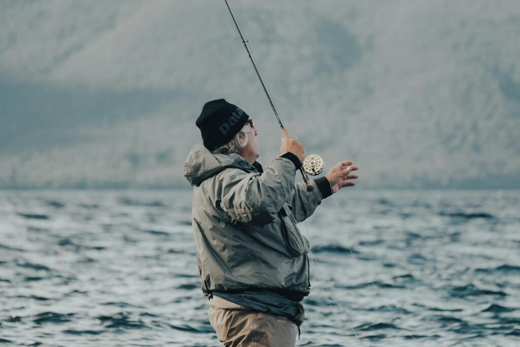 A senior man enjoys a relaxing day fishing on a mountain lake with a fishing rod.