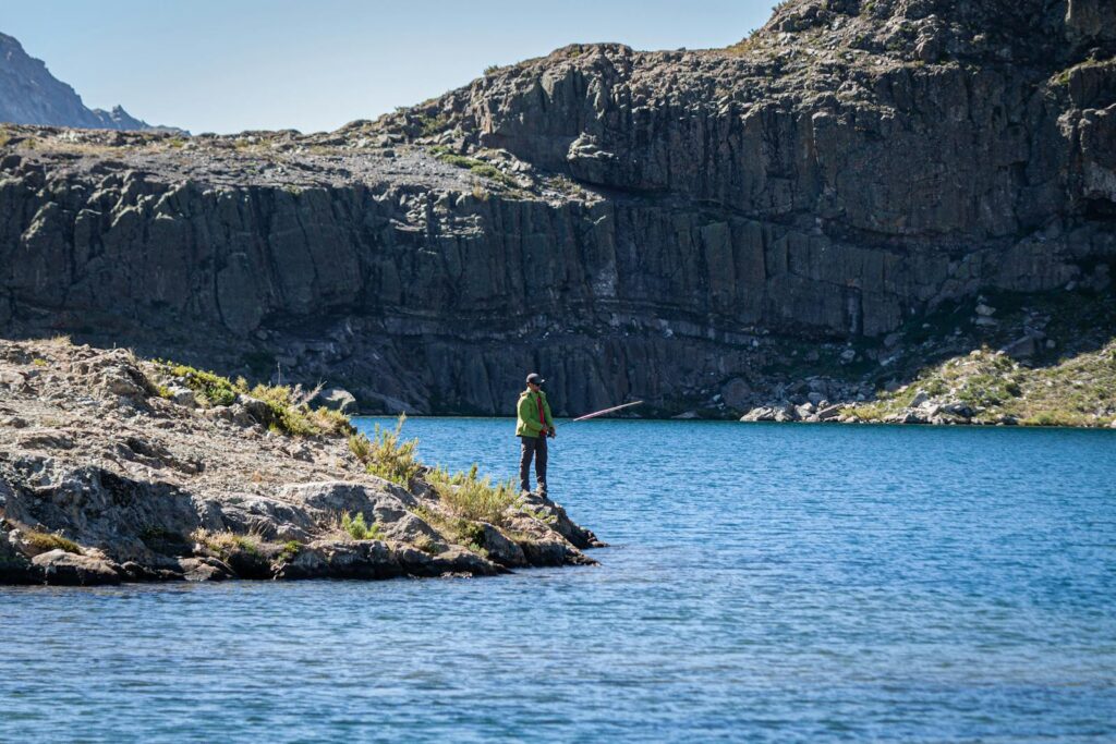 A solitary man fishes by a scenic mountain lake, surrounded by rocky terrain.