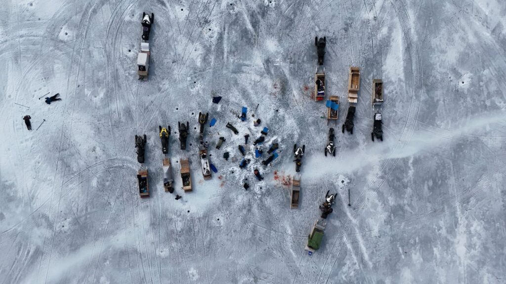 Aerial shot of vehicles and people ice fishing on a frozen lake during winter.