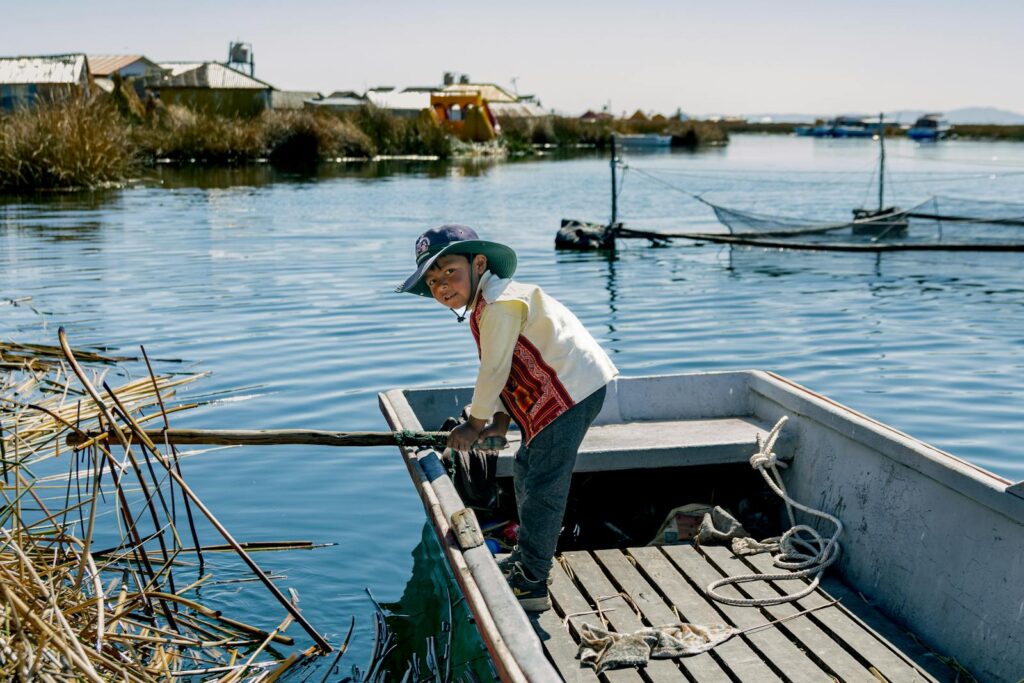 Boy navigating a wooden boat in Puno, Peru on a sunny day. Cultural and scenic vibe.