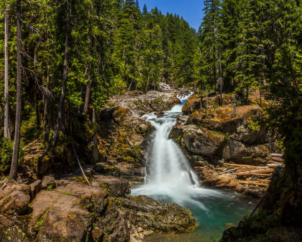 A serene waterfall cascading through a lush green forest with clear blue sky.