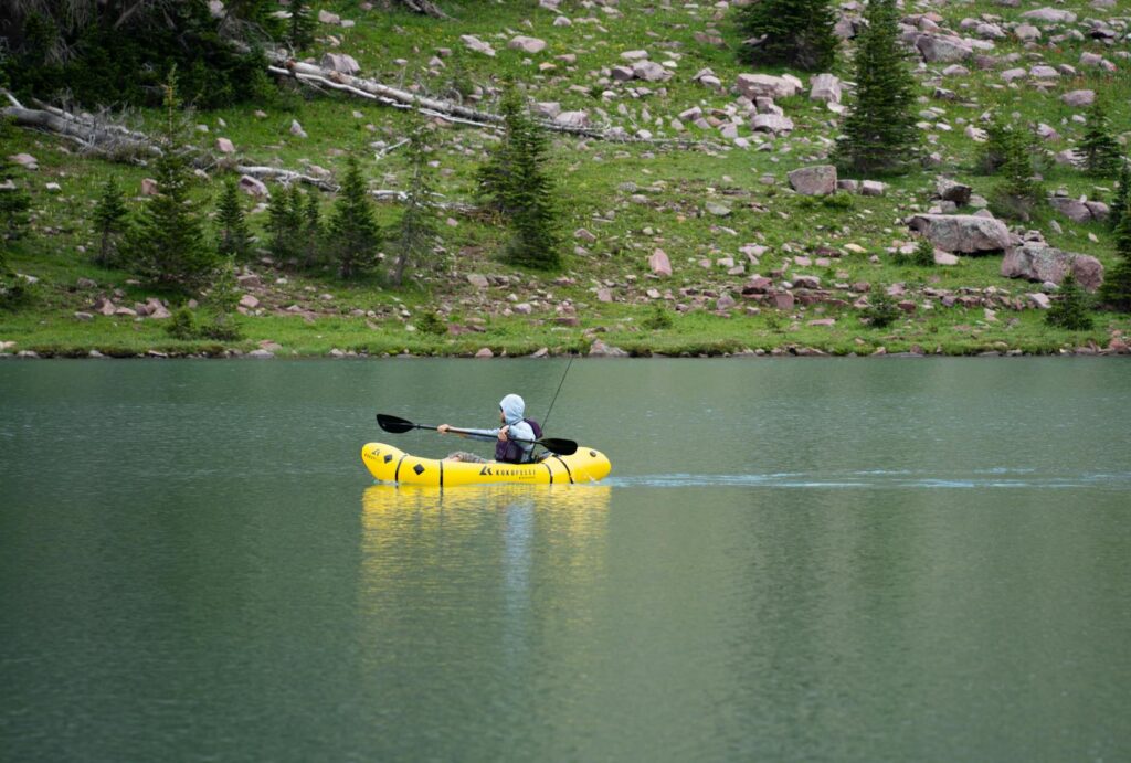A lone kayaker enjoys a peaceful ride on a remote alpine lake surrounded by nature.