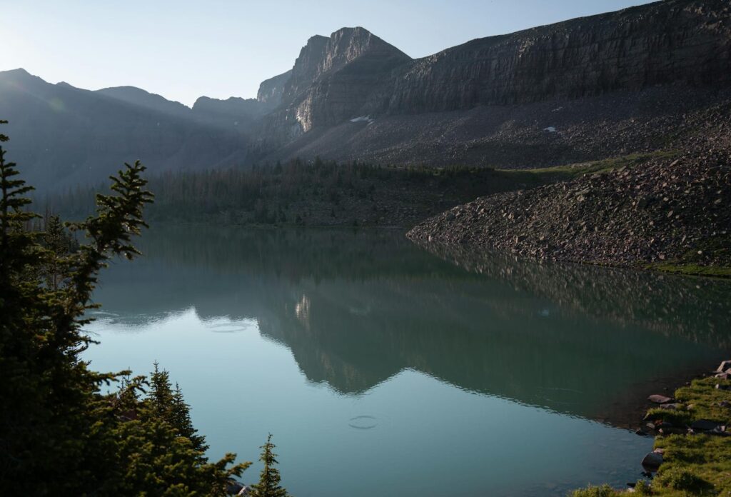 A serene mountain lake with reflections at sunrise, surrounded by a rocky landscape.