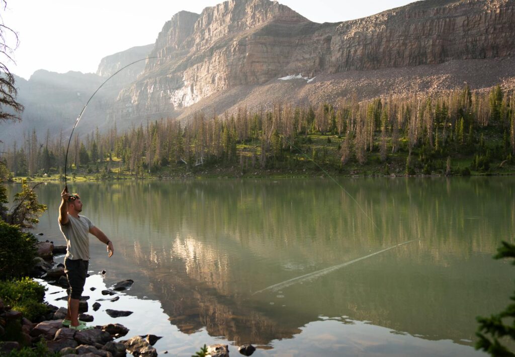 Man fly fishing in serene alpine lake, Utah, with mountain backdrop.