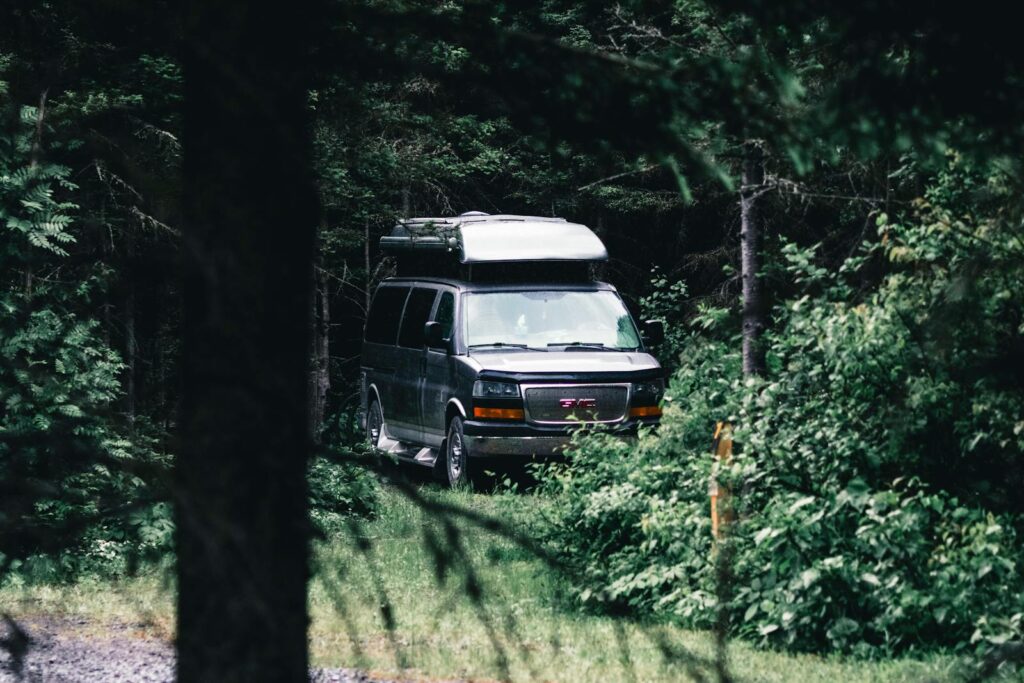 A gray camper van parked amidst lush greenery in Gaspé, Quebec, Canada.