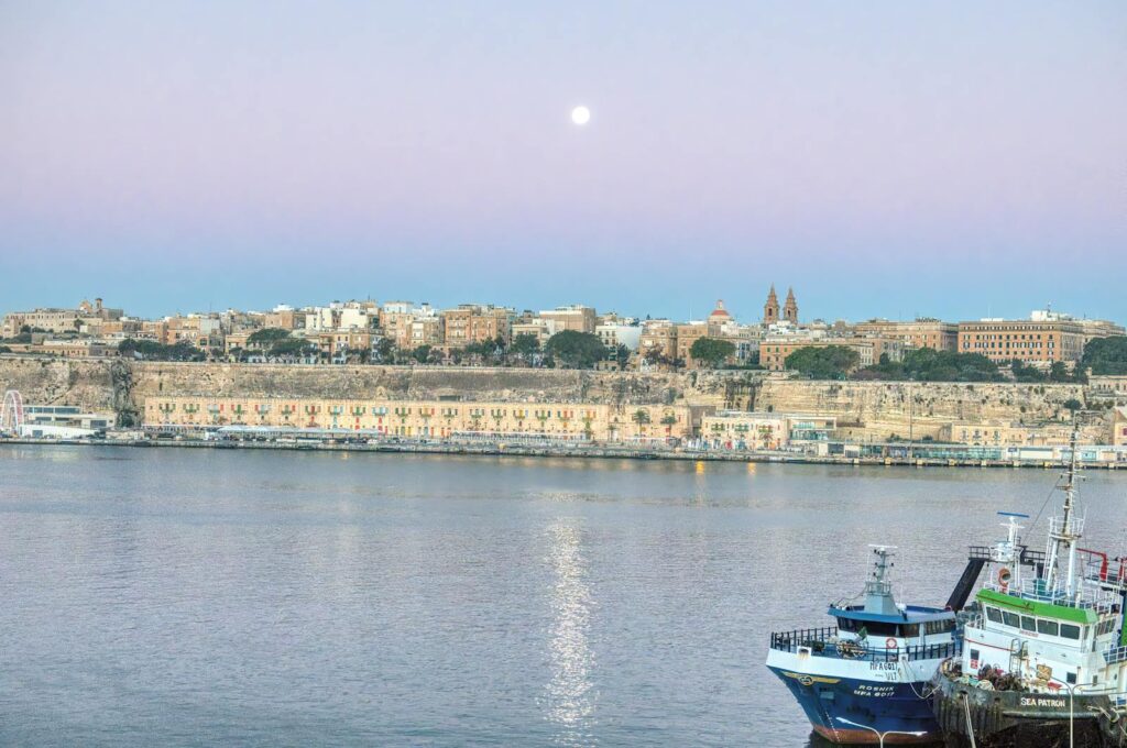 A breathtaking view of Malta's historic cityscape and harbor at sunrise.
