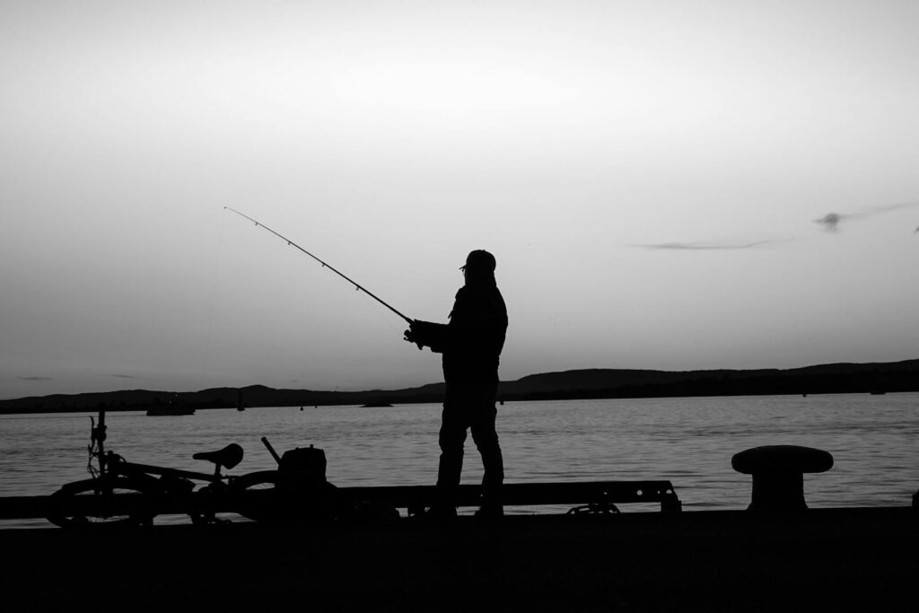 A captivating silhouette of a man fishing during a peaceful sunset at Oslo harbor, Norway.