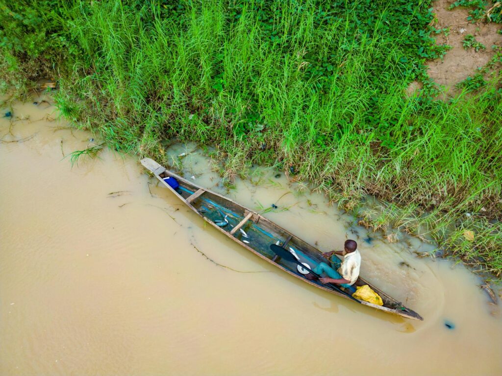 Aerial view of a man canoeing on a muddy river near lush greenery in Kaduna, Nigeria.