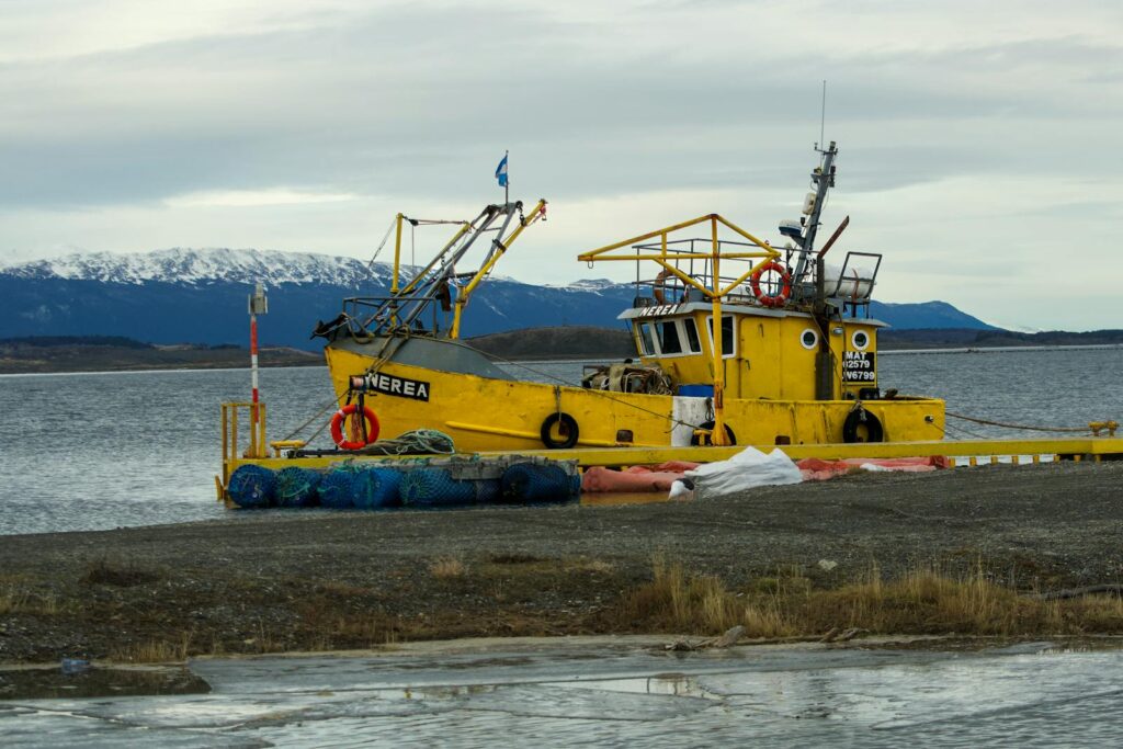 Vibrant yellow fishing boat docked in Puerto Almanza, Argentina with stunning mountain backdrop.