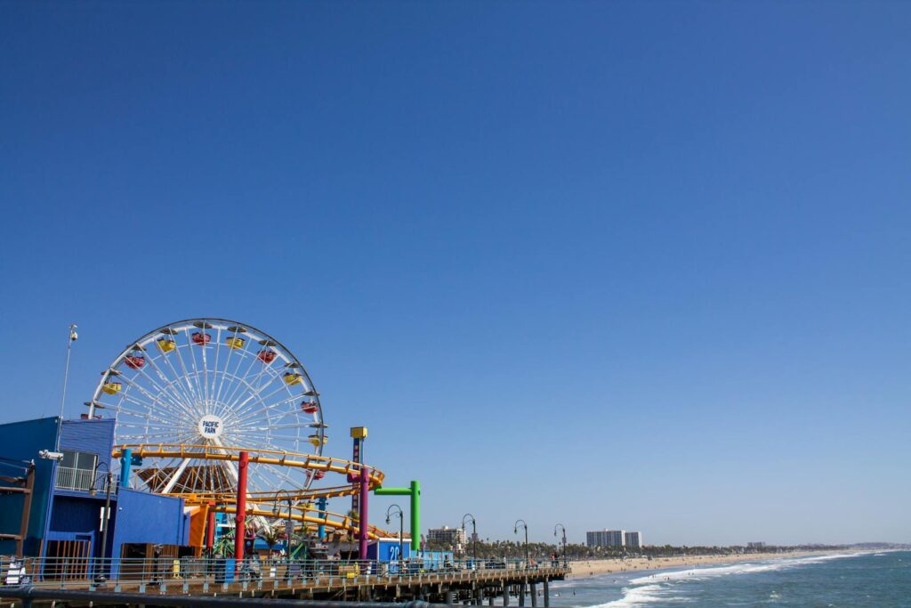 Bright day at Santa Monica Pier featuring the iconic Pacific Park Ferris Wheel against a clear blue sky.