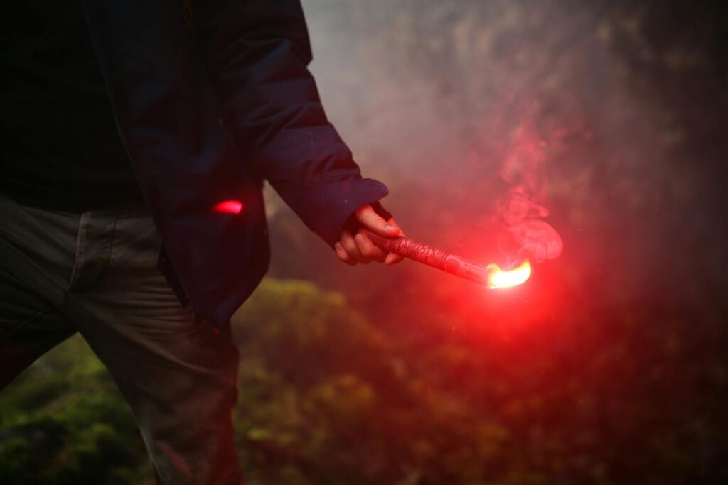 A moody image of a person holding a red flare in an outdoor, smoky environment.