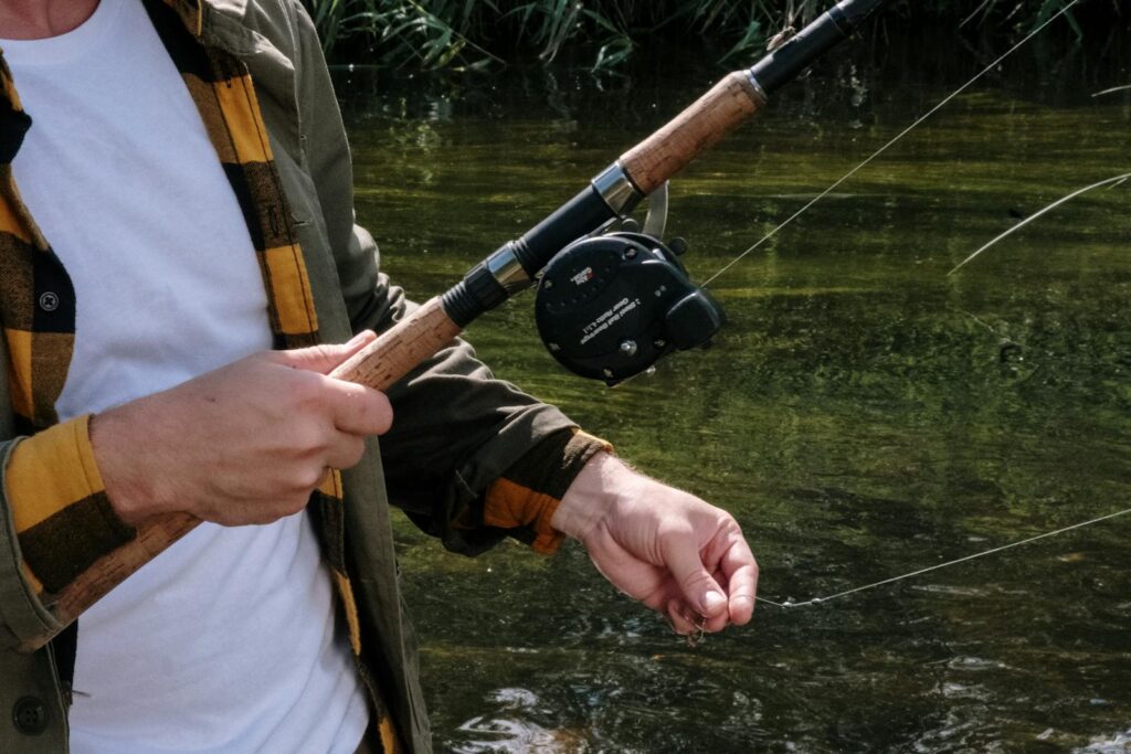Close-up of a man fishing on a tranquil river, showcasing a fishing rod and reel.