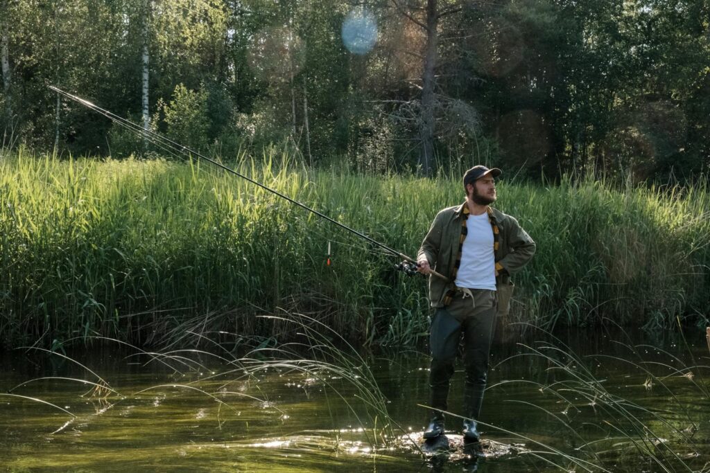 A man enjoys fishing in a peaceful countryside river, surrounded by lush reeds.