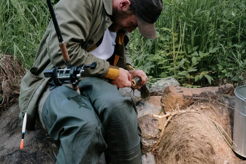 A bearded man fishing outdoors on a summer day in the countryside, preparing his catch.
