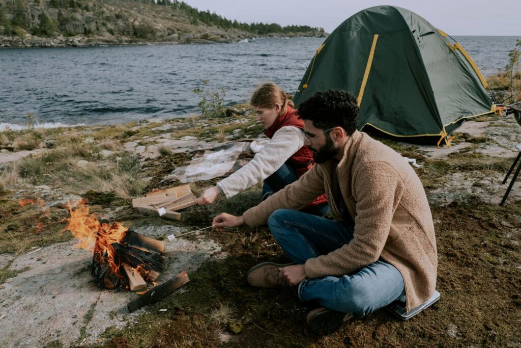 Couple enjoying a peaceful camping trip by a lake, roasting marshmallows by a campfire.