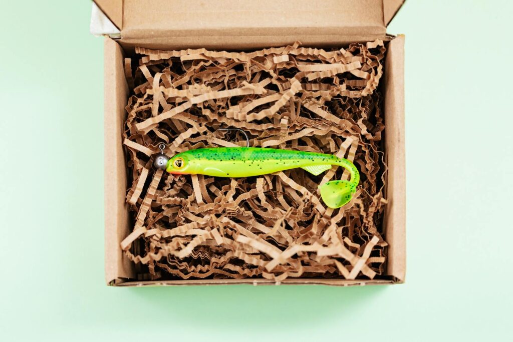 Bright green fishing lure displayed in an open box with shredded paper.