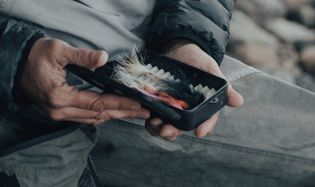 Hands holding a box of colorful fishing lures, ready for angling adventure.