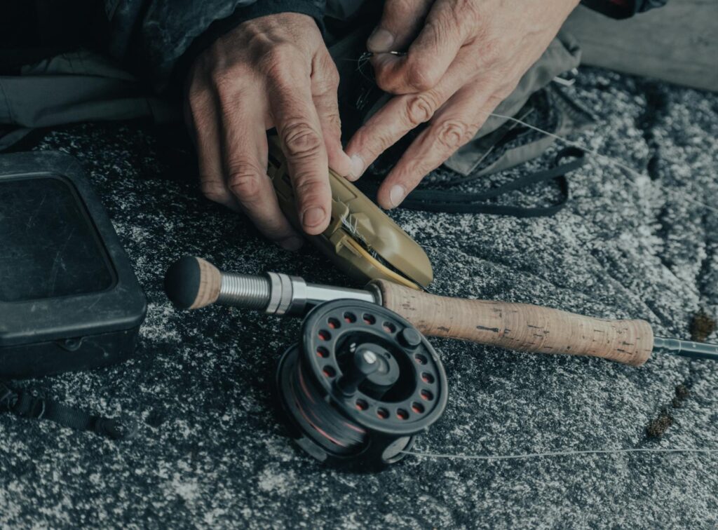 Detailed view of hands setting up a fishing reel with gear on a textured surface.