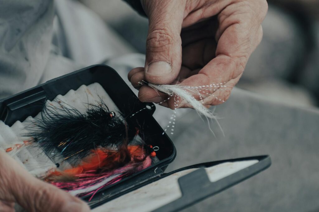 Detailed view of a hand holding a fly fishing lure from a box, depicting preparation for fishing.
