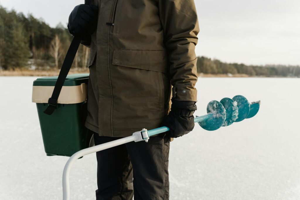 Ice fisherman holding an auger on a frozen lake preparing for winter fishing.