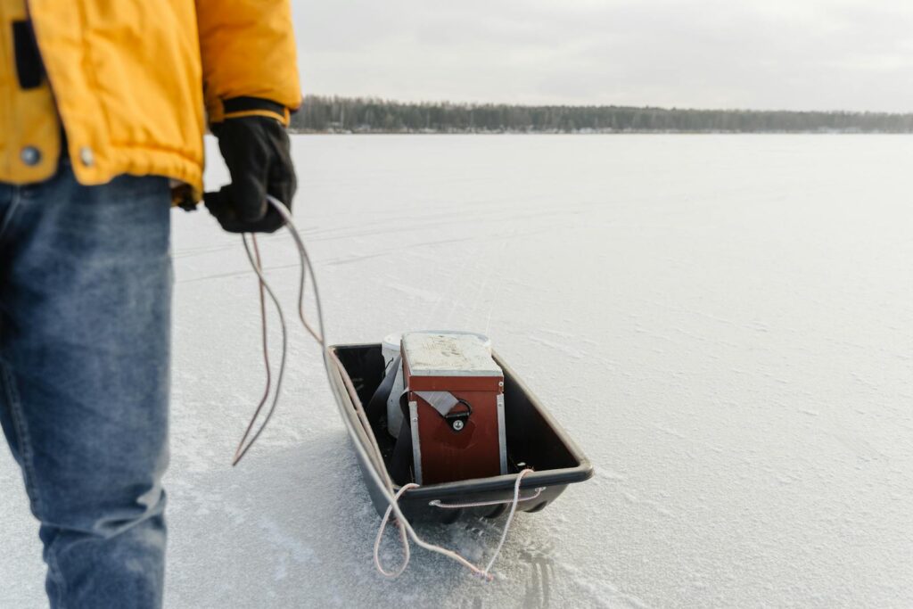 Person pulling sled with fishing gear across a frozen lake during winter.