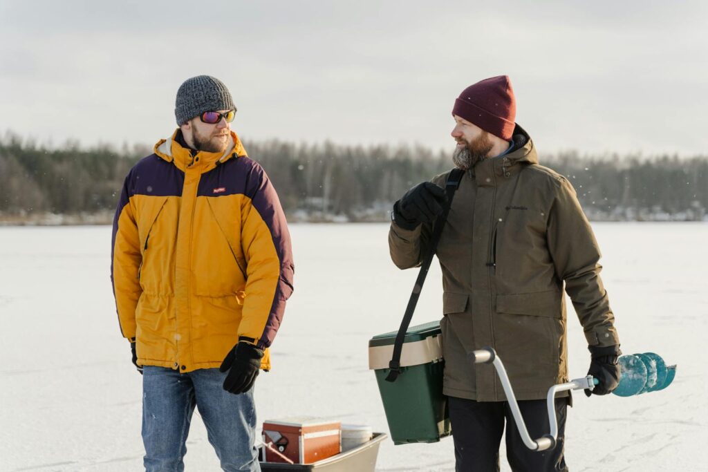 Two men in winter clothes bond while ice fishing on a frozen lake.