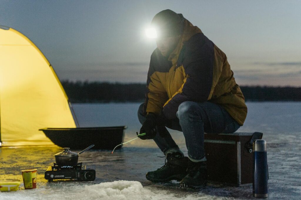 Person ice fishing by a tent on a frozen winter lake, showcasing outdoor adventure and camping experience.
