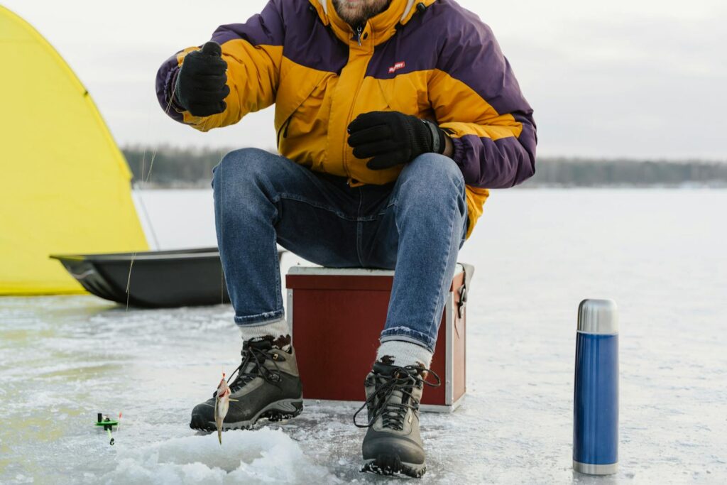 A man enjoying ice fishing on a serene frozen lake during winter, surrounded by gear.