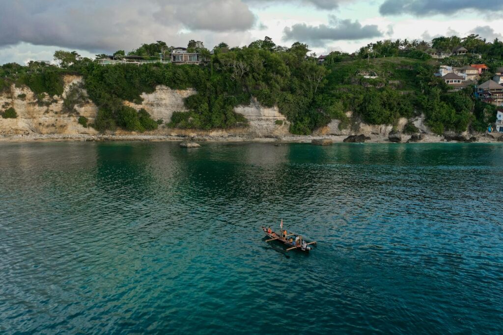 Aerial shot of fishermen in a boat on a calm sea near a cliffside village.