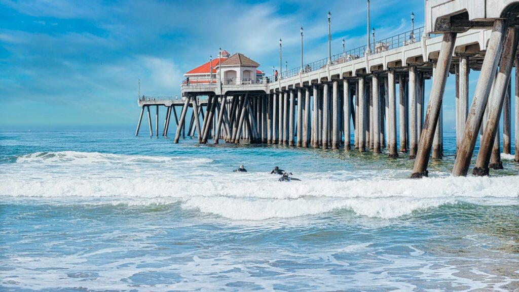 Surfers enjoy waves by the iconic Huntington Beach Pier on a sunny day.