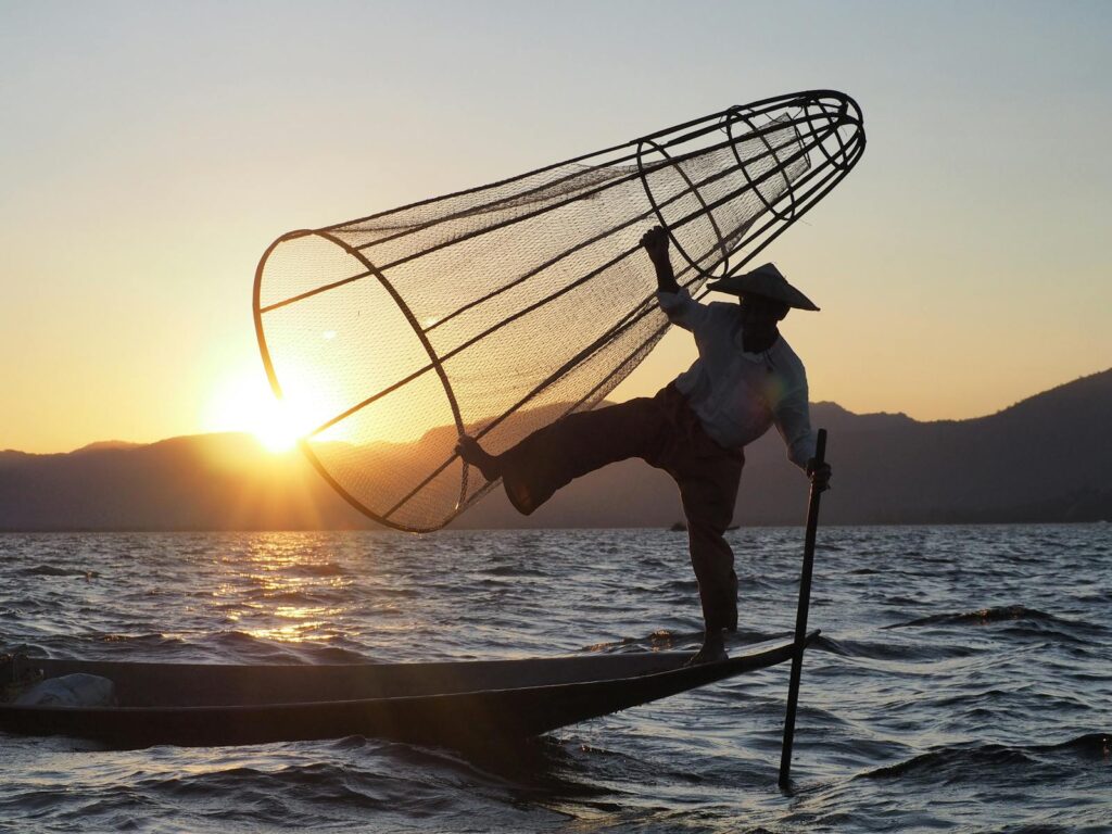 Silhouette of a traditional fisherman balancing on a boat with a net at sunrise on Inle Lake, Myanmar.