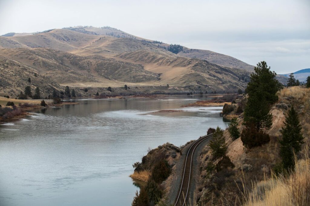 Peaceful river with mountains and railway in Montana's natural landscape.