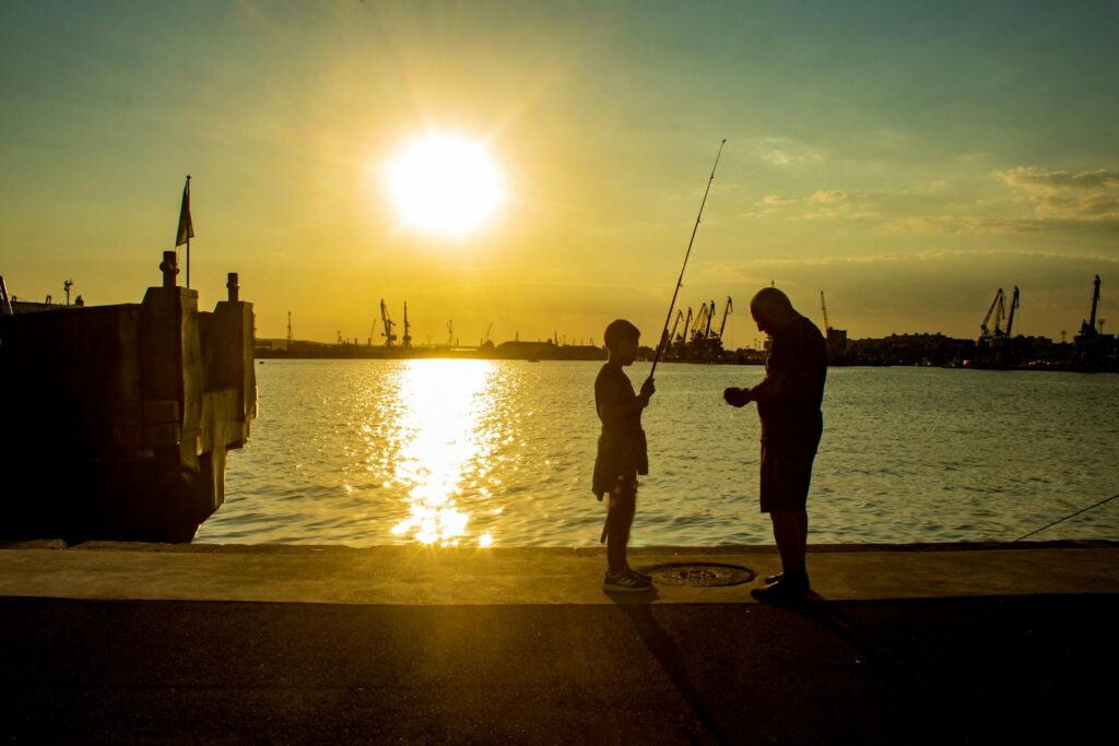 Silhouette of a father and son fishing together at sunset on a peaceful pier.