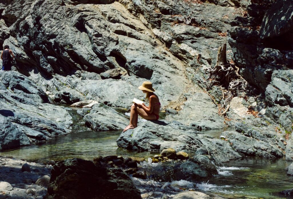 A woman in a bikini reads by a rocky river in Samothraki, Greece.