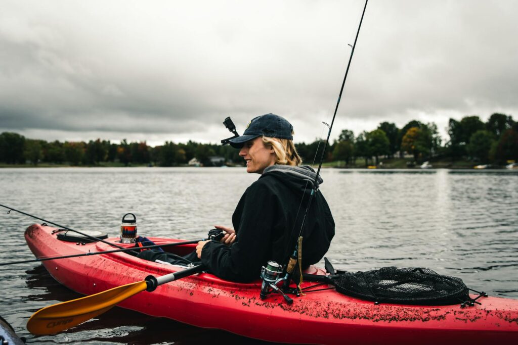 Person fishing from a kayak on a serene lake under overcast skies.