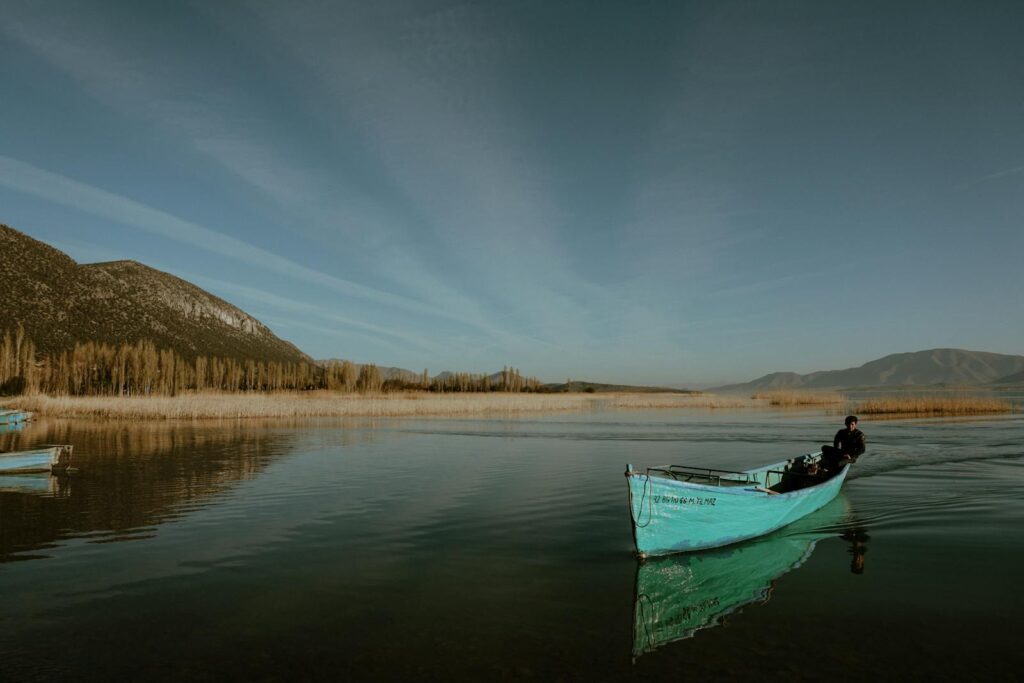 A fisherman navigates a tranquil mountain lake in a blue canoe, reflecting calm waters and scenic mountains.