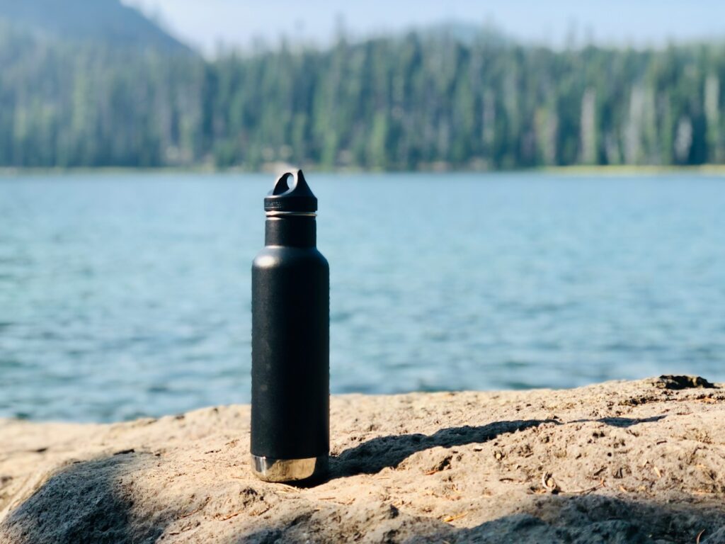 Black and gray sports bottle on brown sand near body of water during daytime.