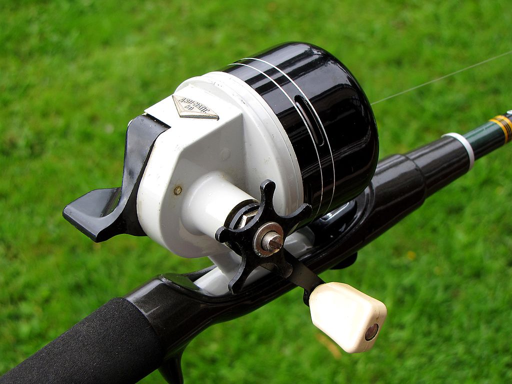 Close-up of a vintage black and white fishing reel on a rod, set against a vibrant green grass background, conveying a sense of nostalgia.