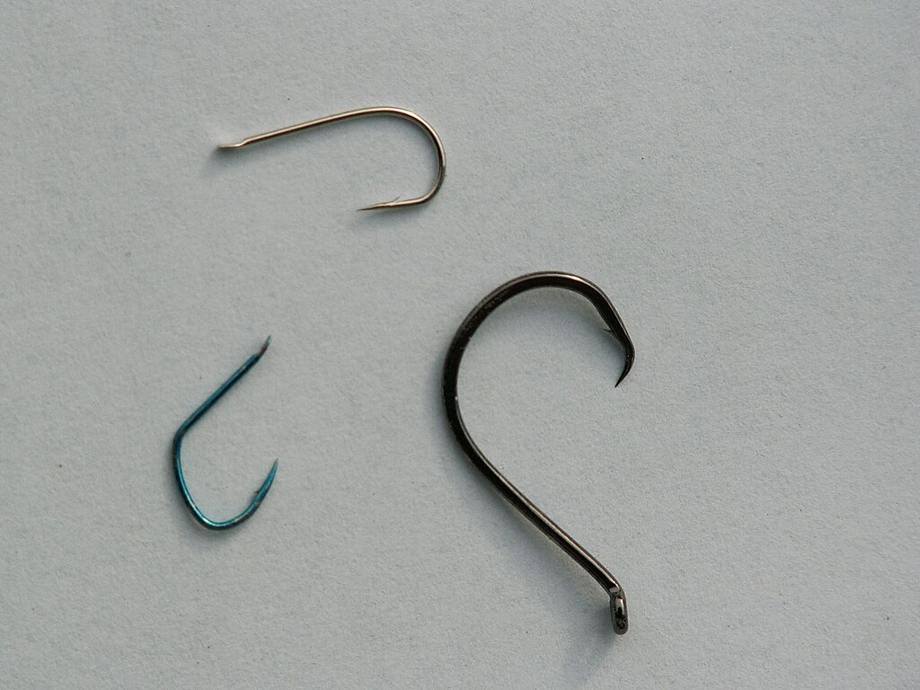 Three fishing hooks are arranged on a plain light grey surface. Varying in size and color, the hooks contrast subtly against the background.